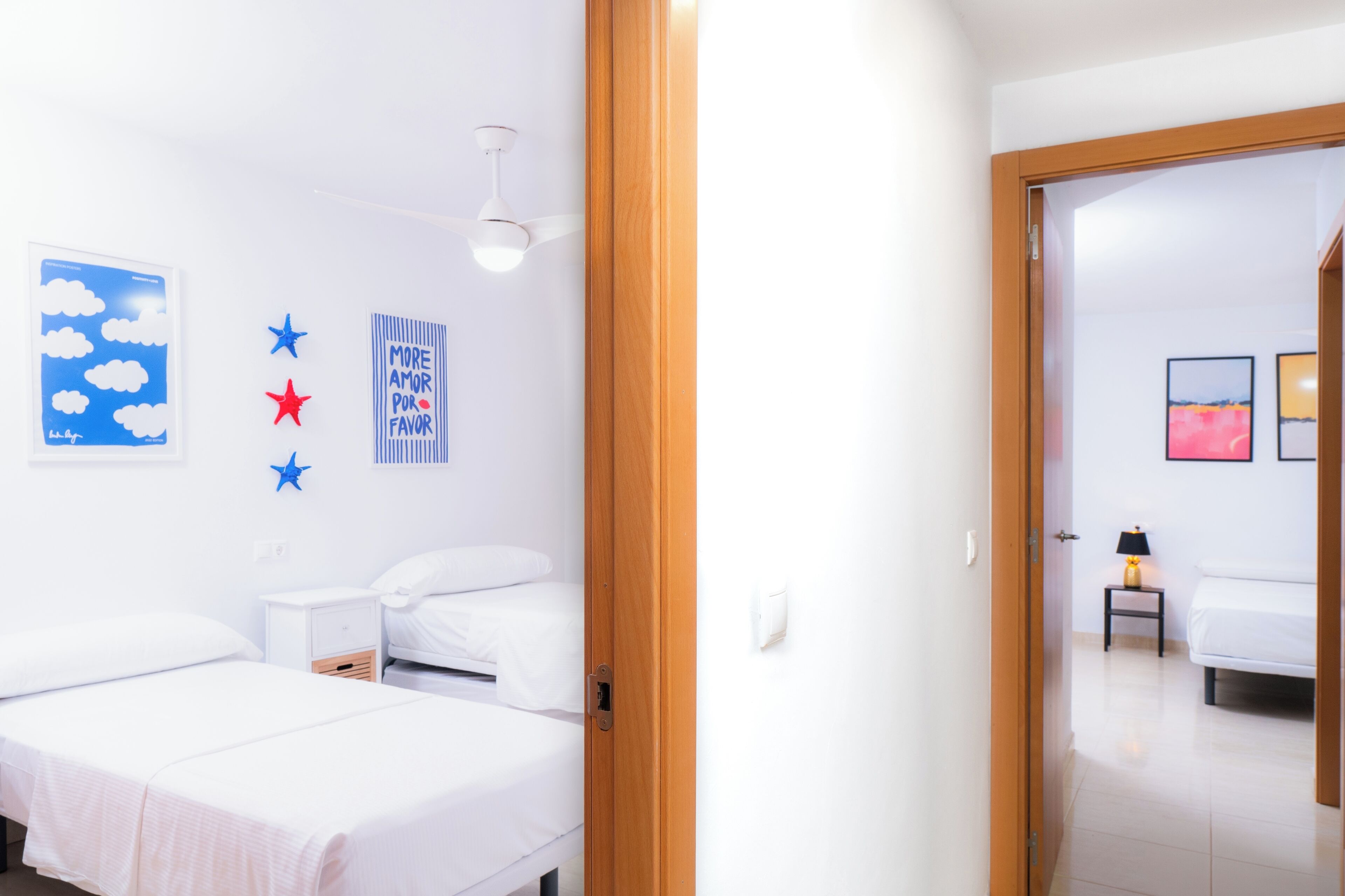 A hotel room with two beds, a ceiling fan, and wall decorations including stars and a cloud painting.