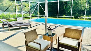 A covered outdoor area with a pool, lounge chairs, and wicker furniture.