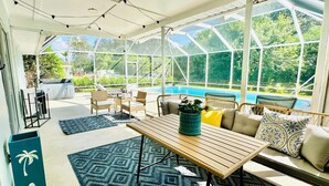 A sunroom with a glass ceiling, a pool, wicker furniture, and a patterned rug.