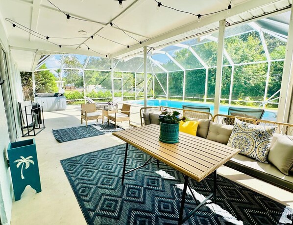 A sunroom with a glass ceiling, a pool, wicker furniture, and a patterned rug.