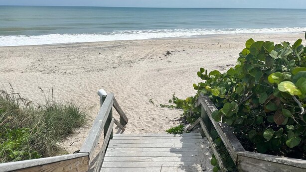 A wooden boardwalk leading to a sandy beach with calm waters and a clear sky.