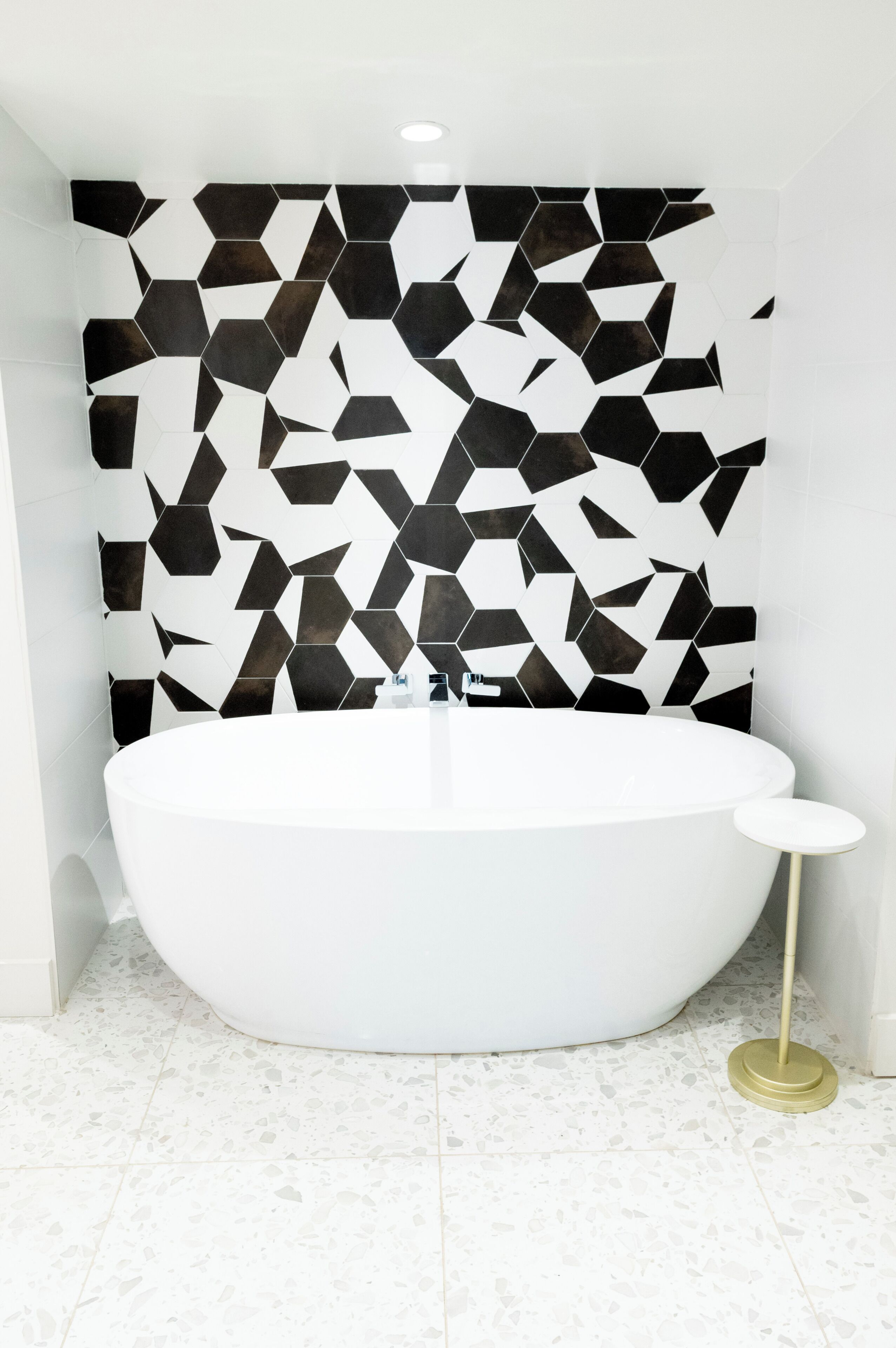 A modern bathroom with a freestanding bathtub, a small round table, and a geometric patterned wall.