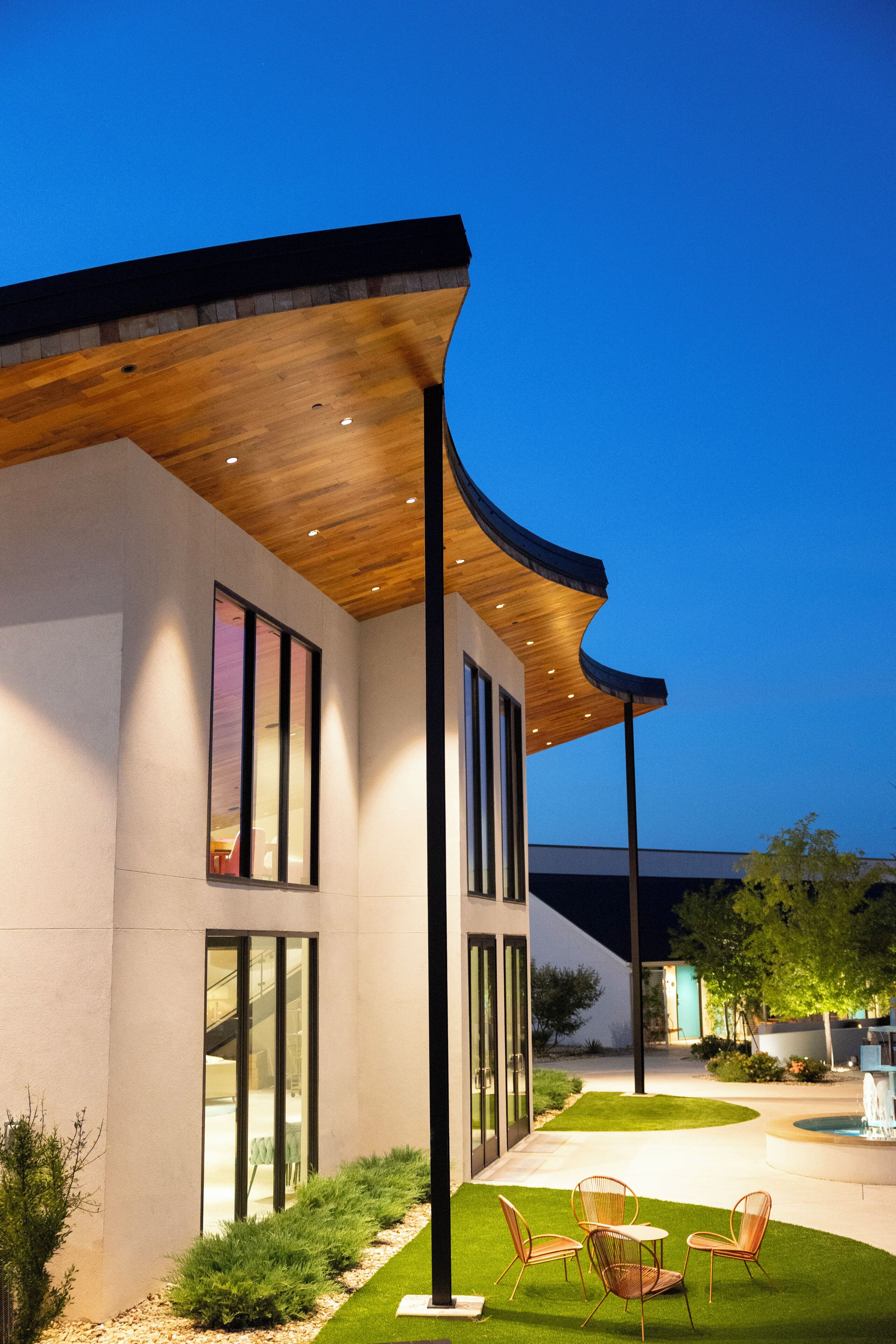 A modern house with a curved roof, large windows, and a well-maintained lawn with outdoor furniture.