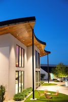 Una casa moderna con techo curvo, ventanas amplias y un césped cuidado con mobiliario de exterior.
