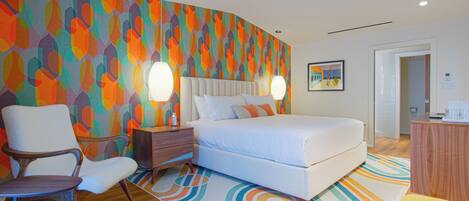 A modern hotel room with a curved wall, a bed, a chair, a nightstand, and a painting.