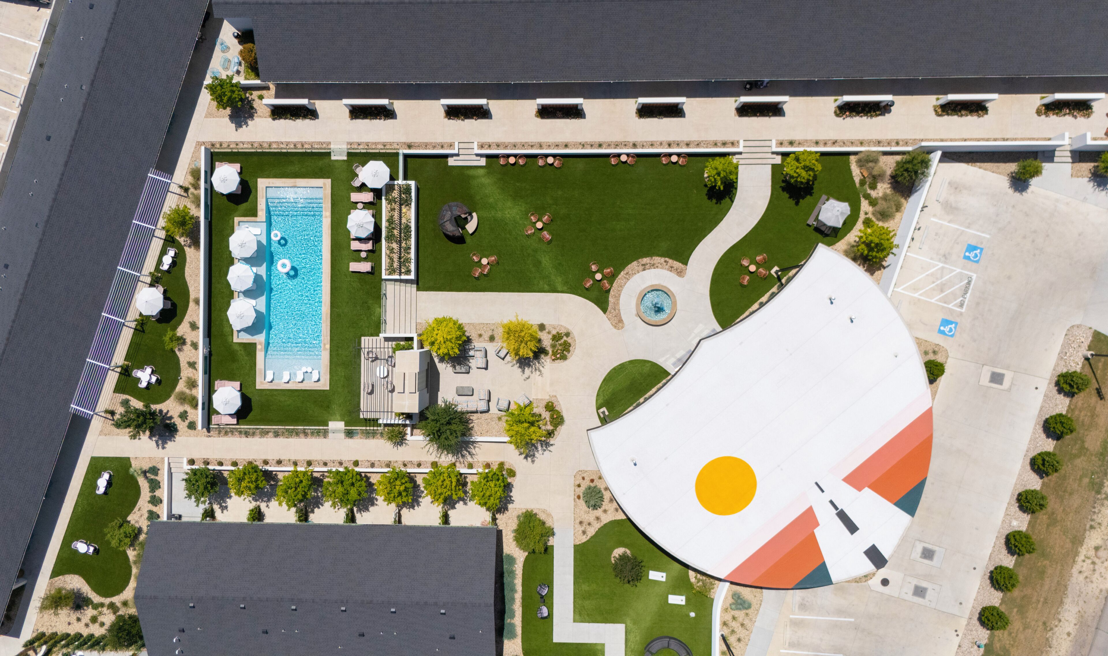 An aerial view of a resort with a swimming pool, lounge areas, and a parking lot.