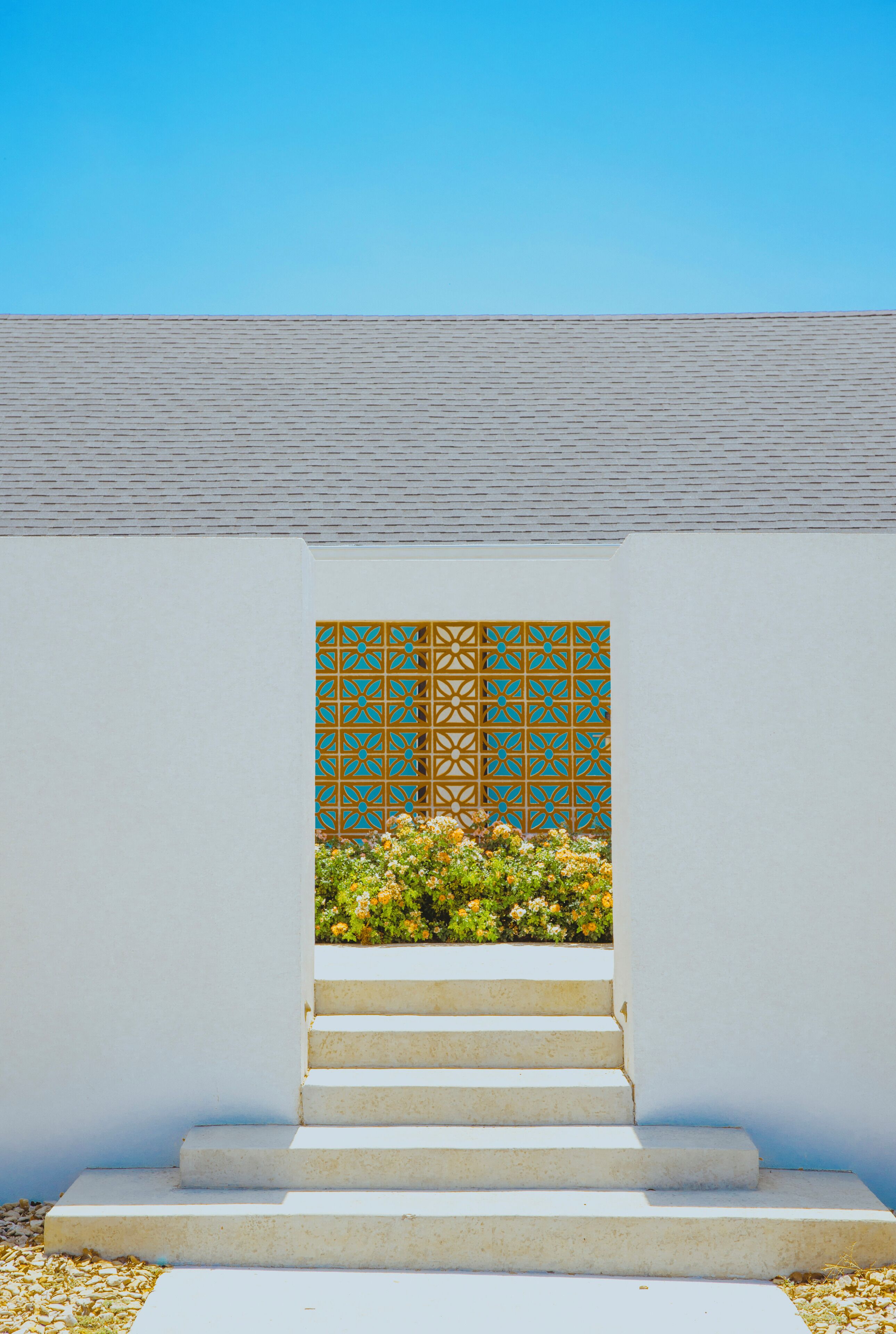 A set of concrete steps leading up to a white wall with a decorative panel and a small garden area with flowers.