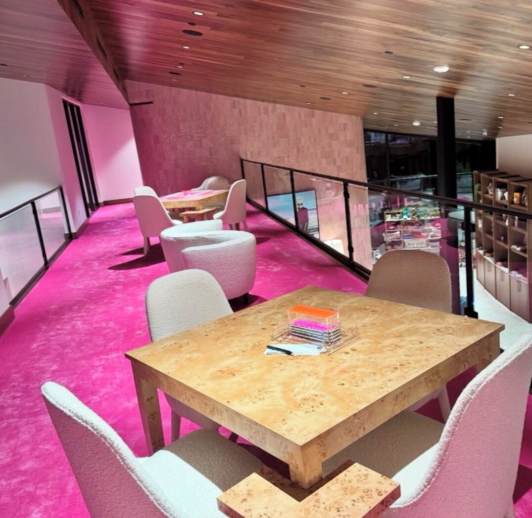 Un interior moderno con alfombra rosa, mesas de madera y sillas blancas.