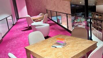 Un interior moderno con alfombra rosa, mesas de madera y sillas blancas.