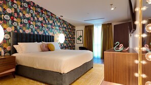 Una habitación de hotel con una cama grande, un tocador con luces y un papel tapiz floral.