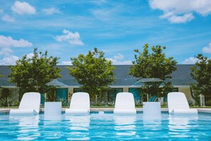 Una piscina con sillas de descanso blancas y árboles al fondo.