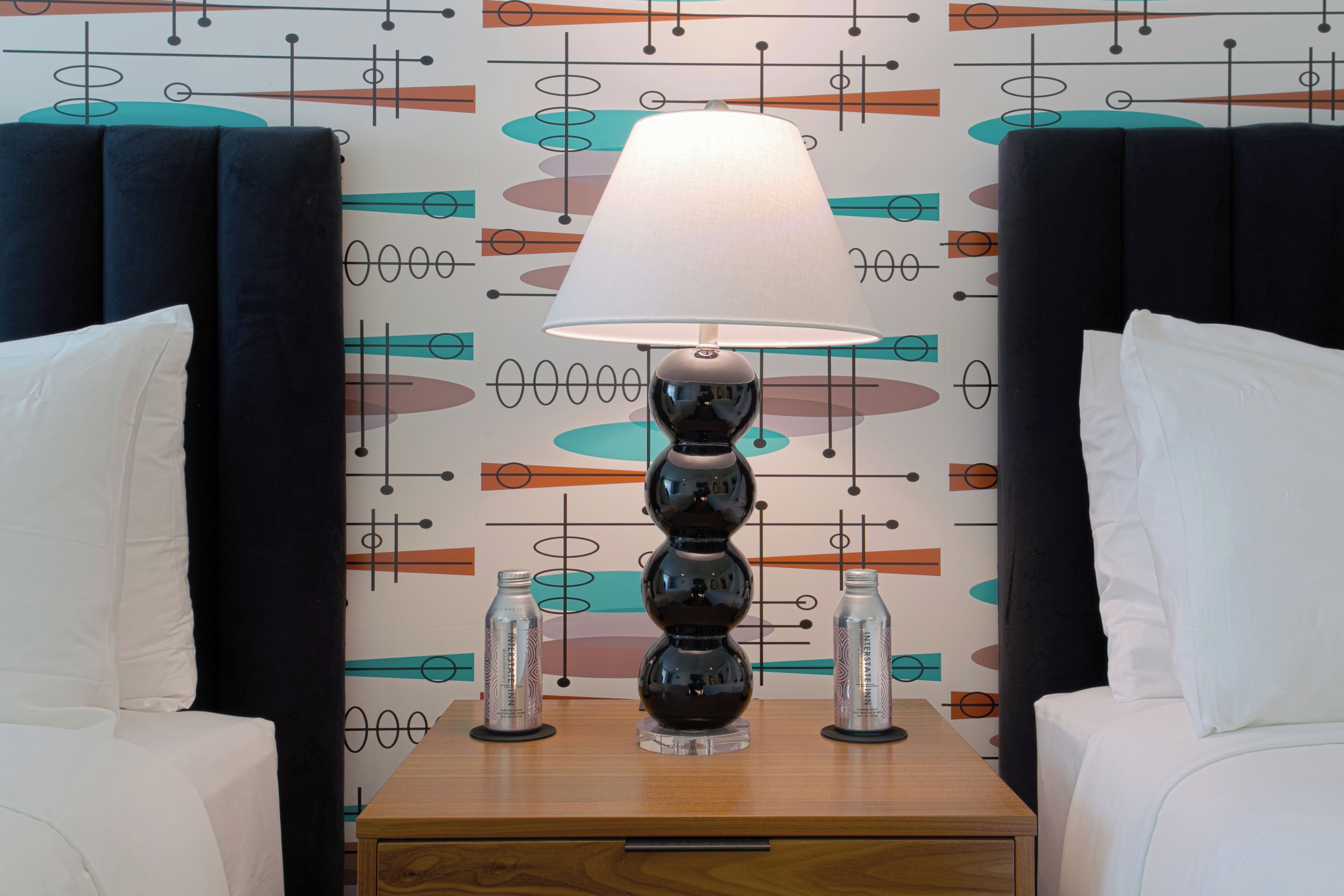Una camera d'albergo con un letto, un comodino con una lampada e una parete decorativa con motivi astratti.