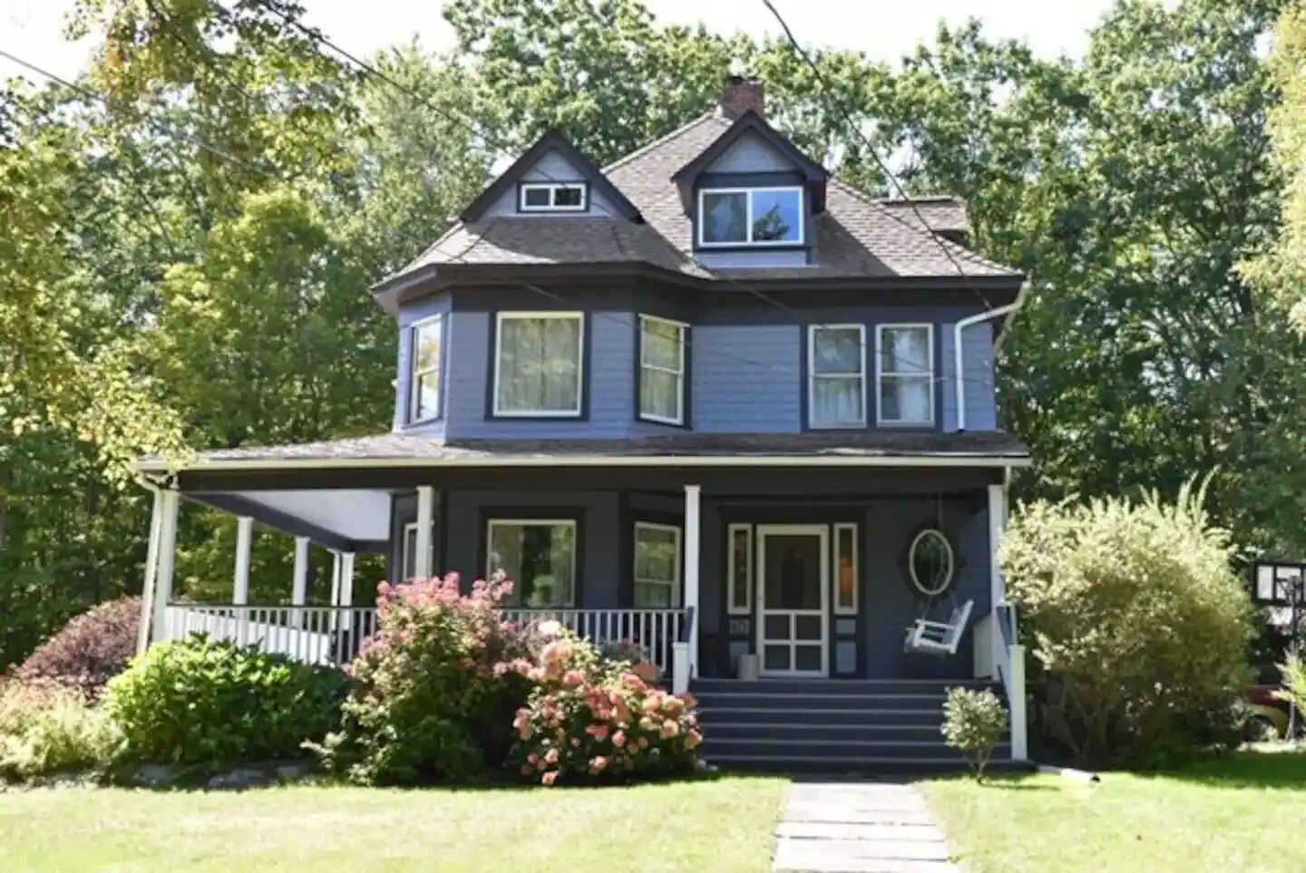 Ein zweigeschossiges Haus mit Veranda, einer kleinen angebauten Garage und einem Vorgarten mit Sträuchern und Blumen.