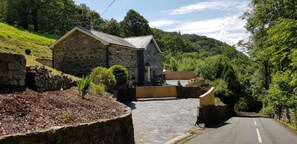 A stone building with a sloped roof, surrounded by a stone wall and a wooden fence. - Snowdonia-3bedroom-2 Bathroom-petfriendly-garden (Blaenau Ffestiniog)
