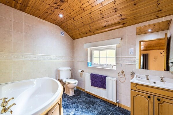 A bathroom with a wooden ceiling, a bathtub, a toilet, a sink, and a window. - Snowdonia-3bedroom-2 Bathroom-petfriendly-garden (Blaenau Ffestiniog)