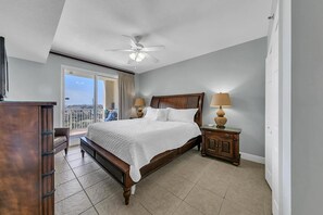 Un dormitorio con una cama grande, ventilador de techo, mesita de noche con lámparas y vista a la ciudad a través de la ventana.