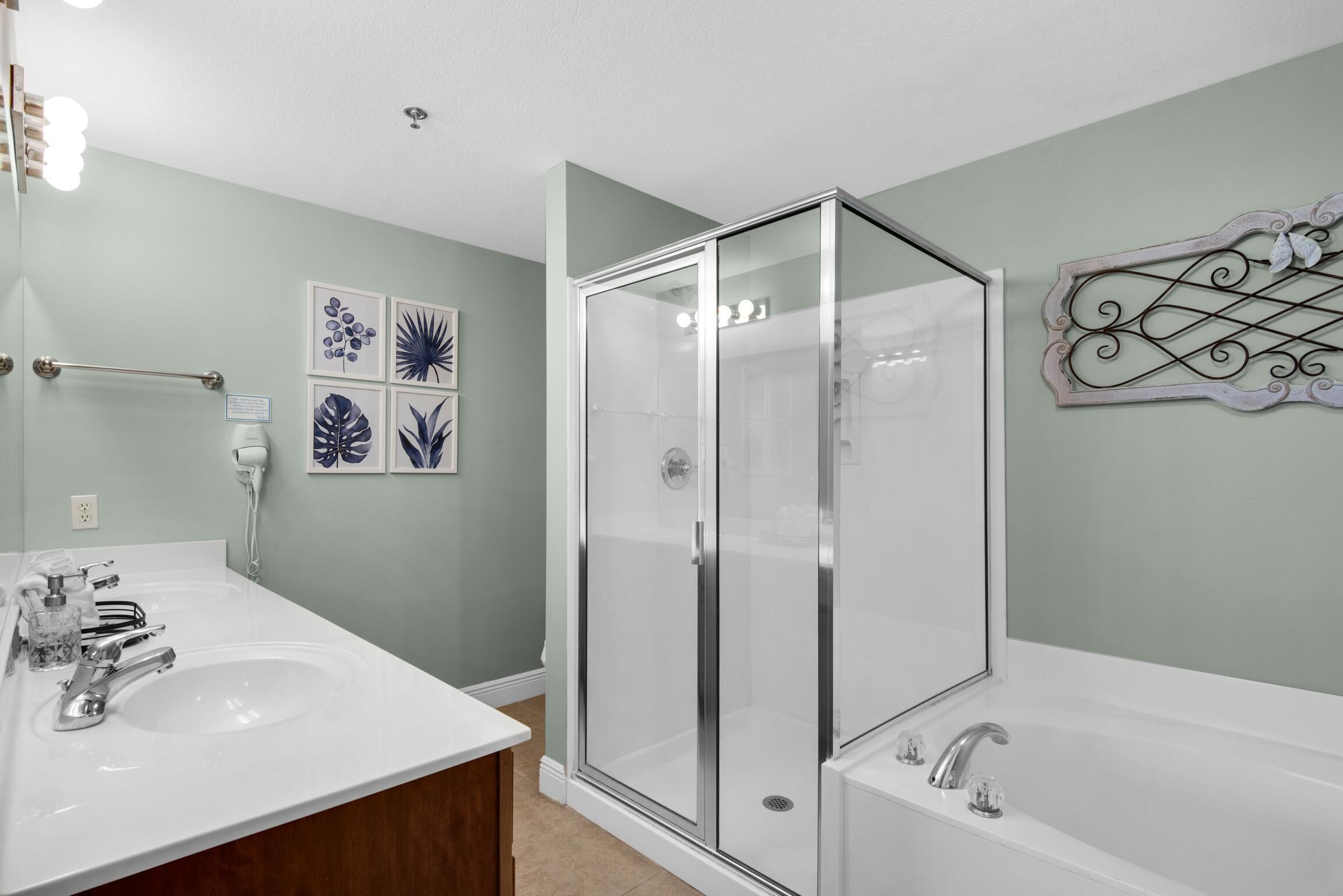 Une salle de bain dotée d’une douche à parois de verre, d’un meuble-lavabo à deux vasques et d’œuvres d’art décoratives murales.