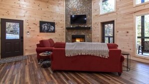 L’intérieur chaleureux d’un chalet avec un canapé rouge, une cheminée en pierre et un téléviseur fixé au mur.