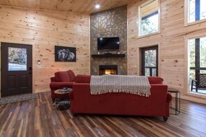 A cozy cabin interior with a red sofa, stone fireplace, and a TV mounted on the wall.