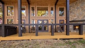 Eine Holzterrasse mit Kamin aus Stein, mehreren Fenstern und Sitzgelegenheiten im Freien.