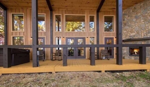 A wooden deck with a stone fireplace, multiple windows, and outdoor seating.