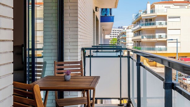 A balcony with a wooden table and chairs, a potted plant, and a view of the cityscape. - Edifico Tramontana (Peniscola)