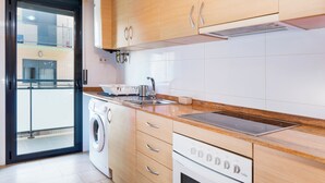 A modern kitchen with wooden cabinets, a built-in washing machine, and a stainless steel sink. - Edifico Tramontana (Peniscola)