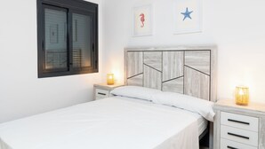 A bedroom with a bed, two bedside tables, a window, and wall art. - Edifico Tramontana (Peniscola)