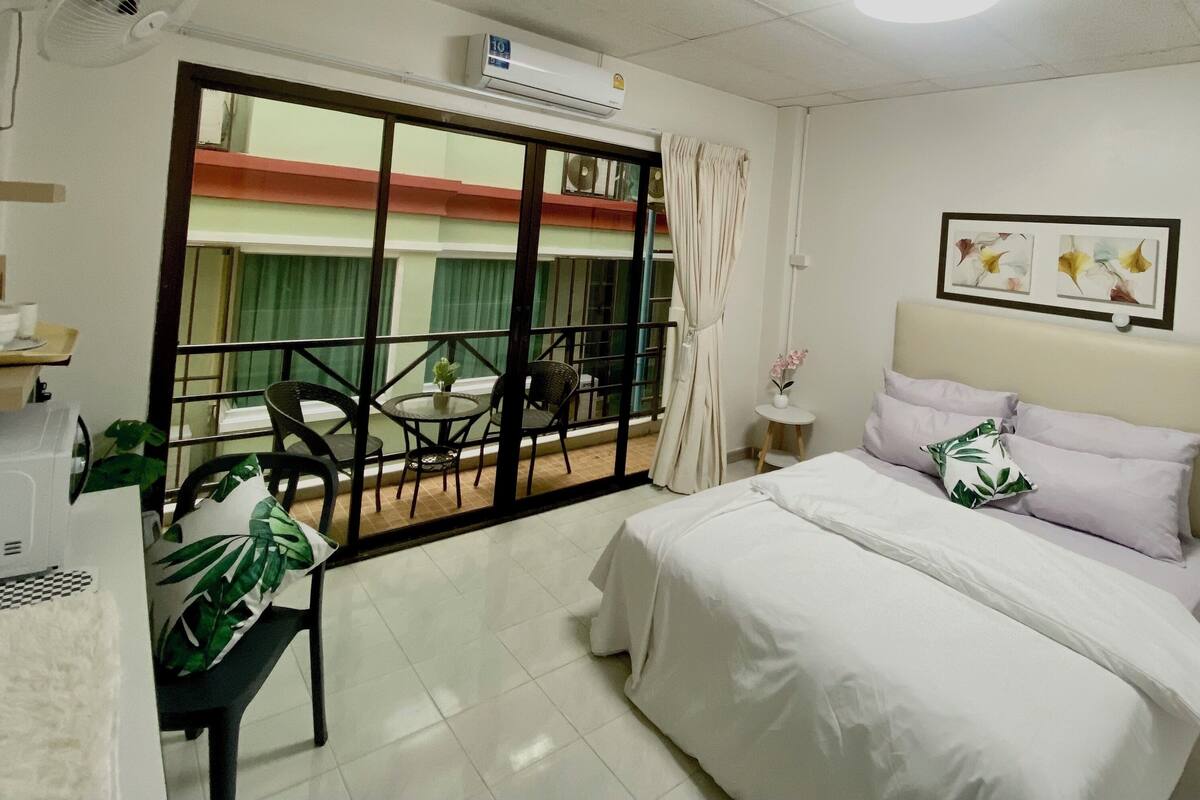 Habitación de hotel con cama, una mesita con sillas, ventana con vista a edificios y un equipo de aire acondicionado.