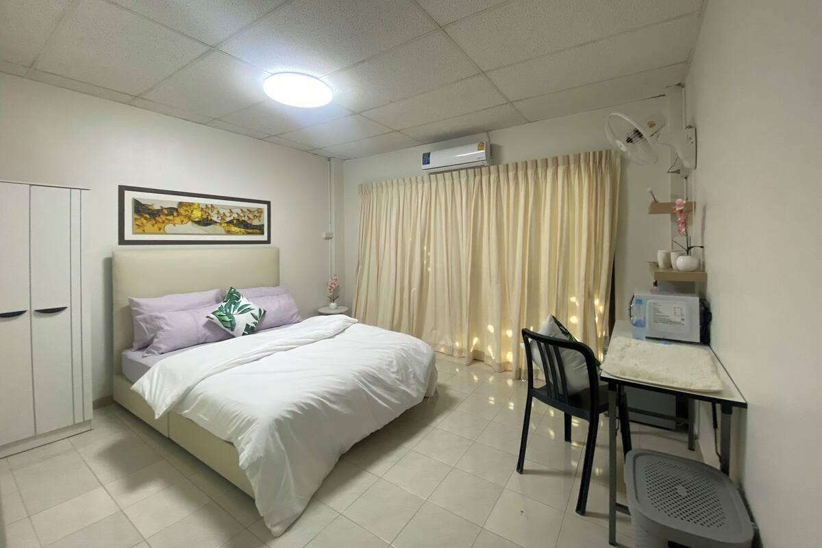 Una habitación de hotel con cama, escritorio, silla, aire acondicionado y un cuadro en la pared.