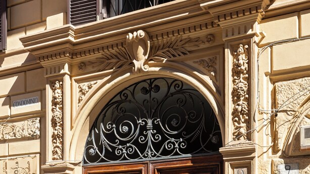 Una porta doble de fusta amb un tirador de bronze, situada en un edifici beig amb detalls arquitectònics ornamentals.