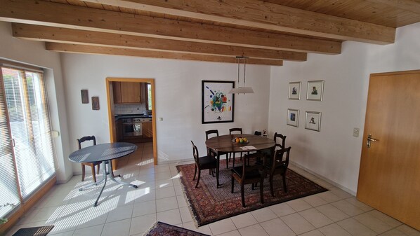 Un comedor con mesa y sillas de madera, una cocina al fondo y una puerta a la derecha.