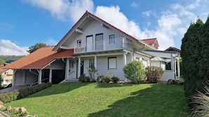 A two-story house with a red-tiled roof, a balcony, and a covered porch. - Living on the golf course in a very quiet location.  (Haarbach)