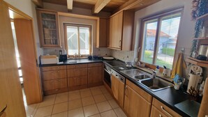 A kitchen with wooden cabinets, a stove, a sink, and a window with blinds. - Living on the golf course in a very quiet location.  (Haarbach)