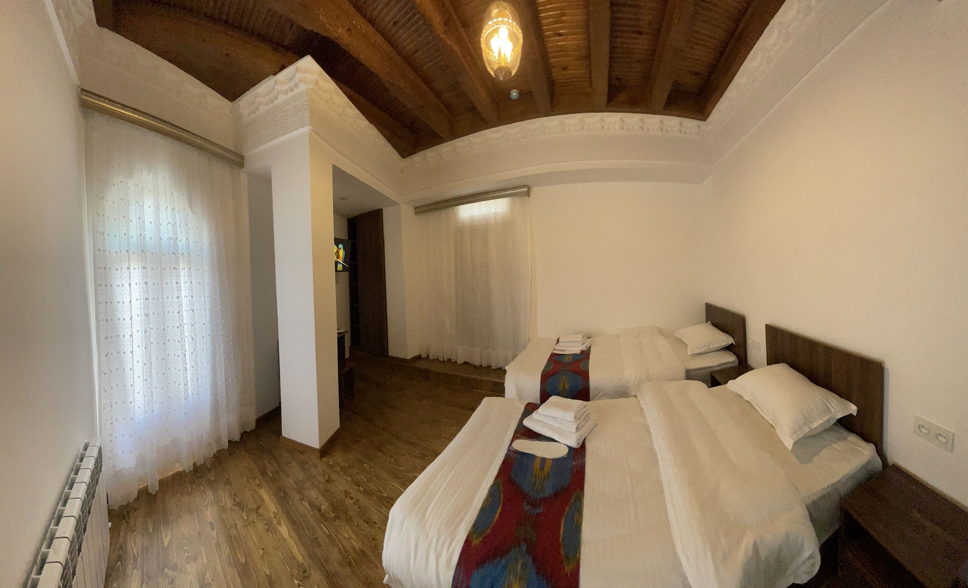 Una habitación con dos camas, suelo de madera, techo con vigas a la vista y ventana con cortinas.
