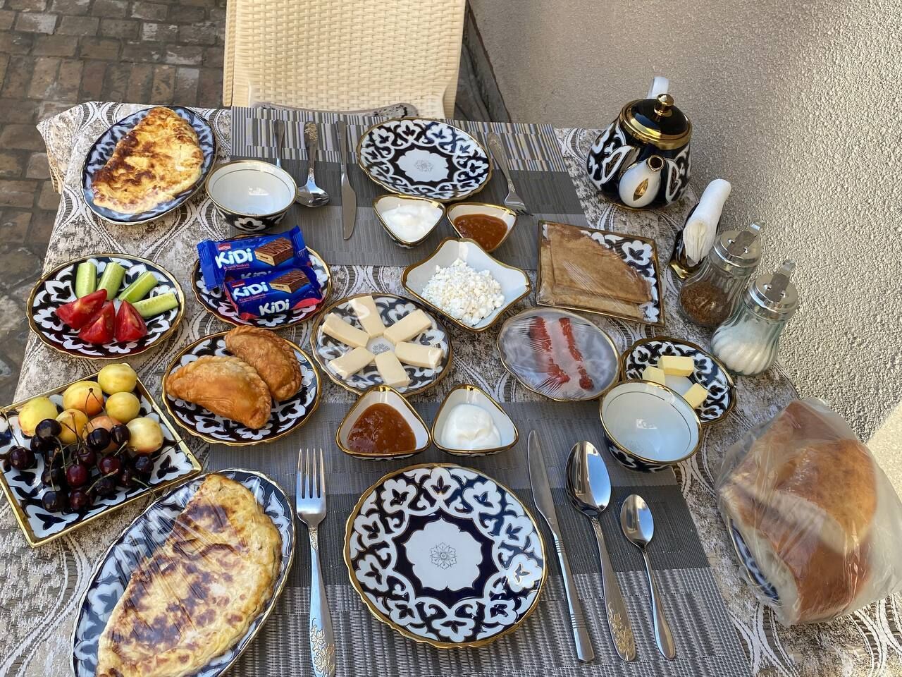 A table set with various dishes, including fruits, cheeses, and bread, suggesting a meal setup outdoors.