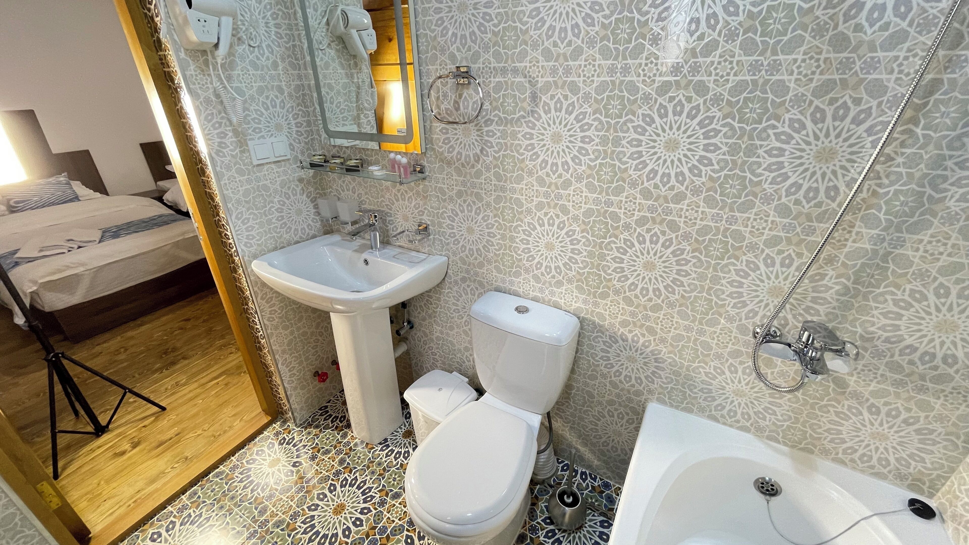 A bathroom with a sink, toilet, and bathtub, featuring patterned tiles and a wooden floor.