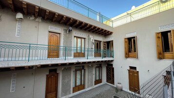 Un patio con balcón de madera, piso de baldosas y puerta tradicional de madera.