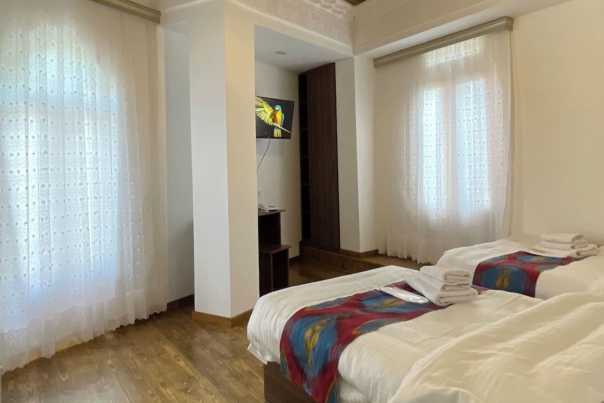 A room with wooden flooring, a bed with white bedding, a wooden ceiling, and a television mounted on the wall.