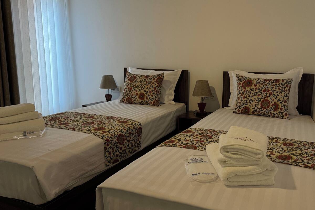 Two single beds with floral-patterned bedspreads and matching pillows, a small table with a lamp, and a stack of folded towels.