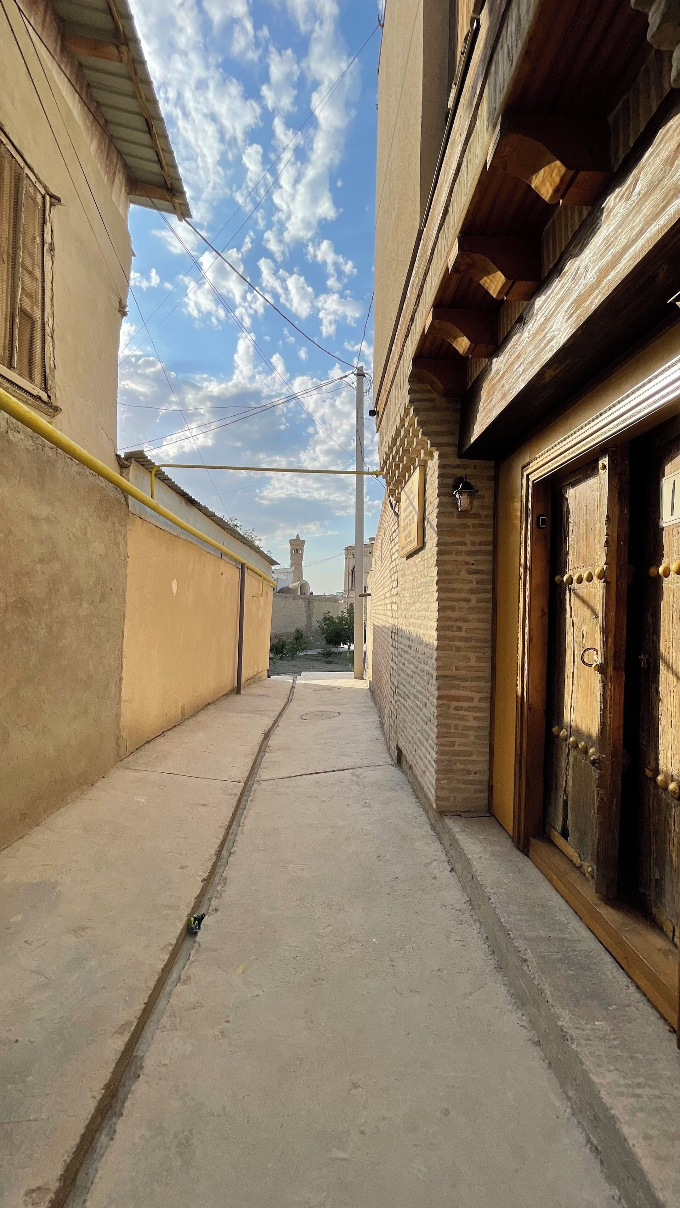 Une ruelle étroite entre deux bâtiments, avec un ciel dégagé et une tour qui se profile au loin.