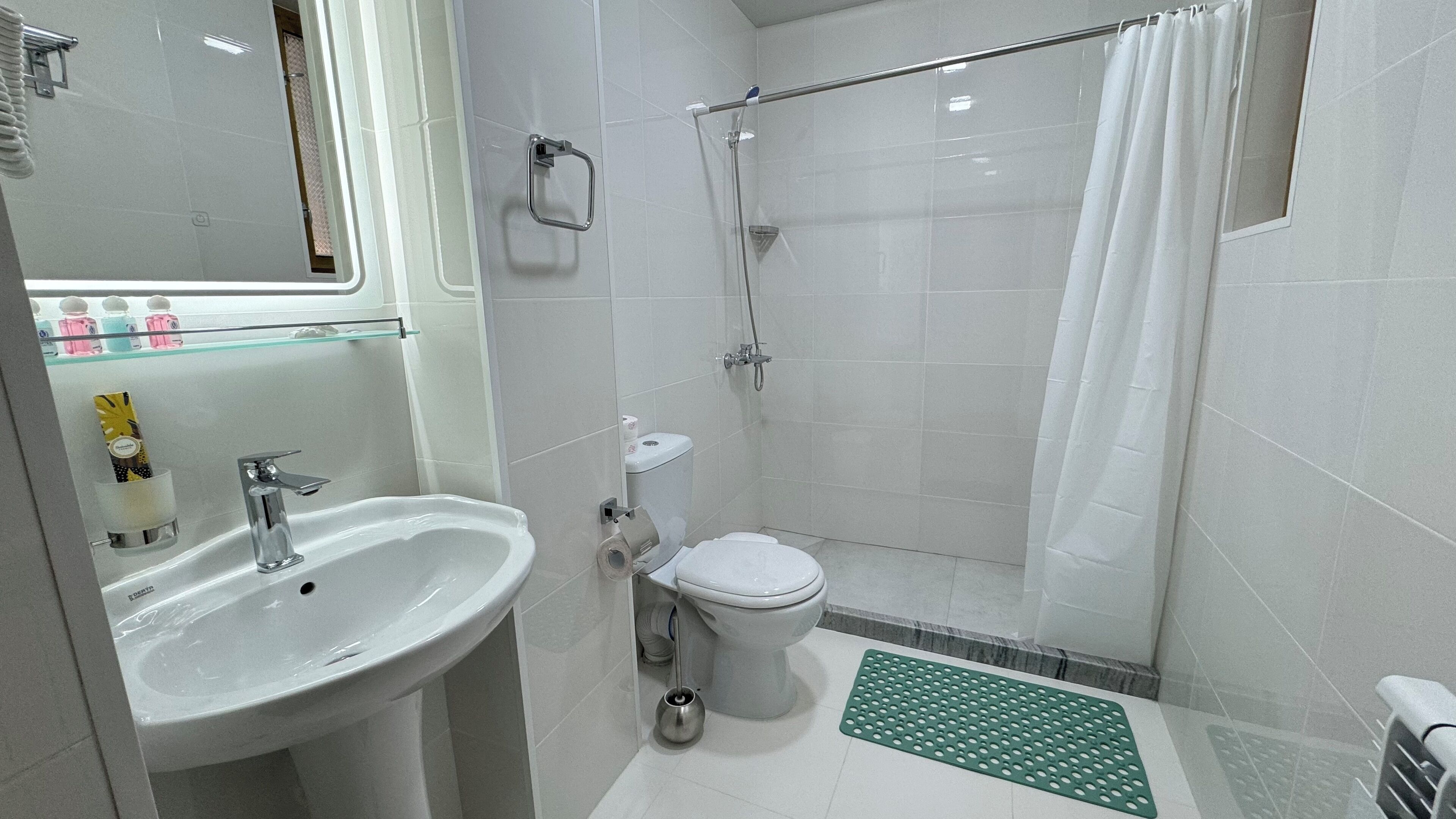 A bathroom with a sink, toilet, shower, and a glass shelf with toiletries.