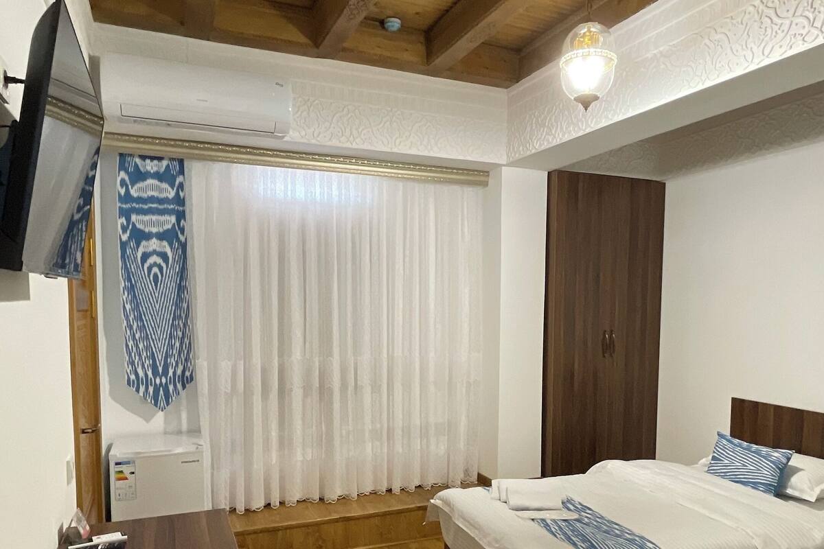 A bedroom with two beds, wooden flooring, a TV on a stand, and a ceiling with exposed beams.