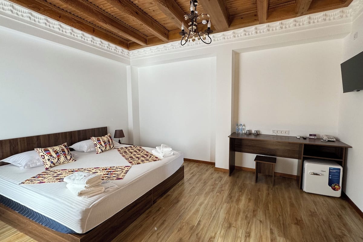 A bedroom with a wooden bed, a desk, a chair, a television, and a minibar.