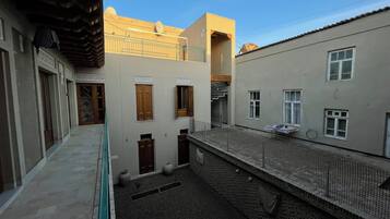 Une ruelle étroite, bordée de bâtiments des deux côtés, qui mène à une petite cour intérieure agrémentée d’une clôture en métal, d’un sol carrelé et de quelques fenêtres.