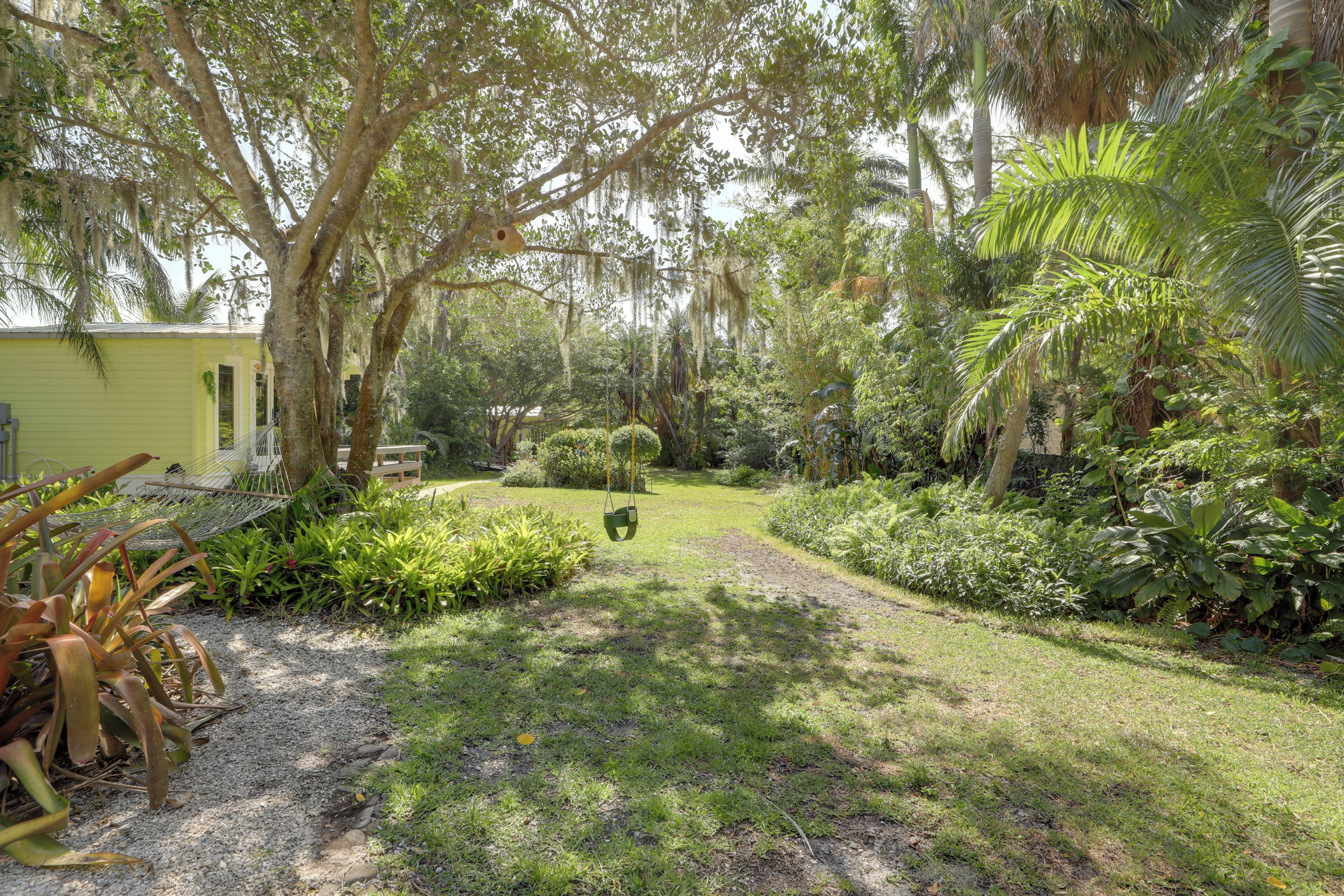 Un exuberante jardín con una hamaca, un edificio amarillo y diversas plantas tropicales.