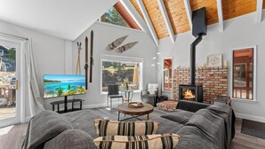 A modern living room with a large TV, comfortable seating, a fireplace, and a scenic view.