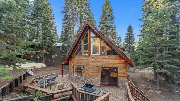 A cabin with a deck, outdoor seating, and a grill area.