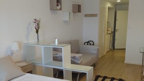 Une chambre moderne avec un lit, une table de chevet et un petit bureau avec une chaise. On y trouve une porte donnant sur une autre pièce et un couloir.