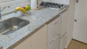 Une cuisine avec des meubles blancs, un plan de travail en granit, un four encastré, une cuisinière à gaz et un évier.